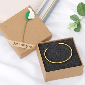 Gros plan d'un bracelet doré gravé FOREVER dans un coffret cadeau en papier kraft