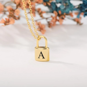 Detail of a gold padlock pendant with letter A engraving on a minimalist chain