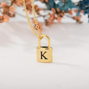 Macro shot of a gold padlock pendant necklace with engraved letter K and fine cross chain