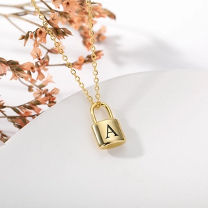 Detailed view of golden padlock necklace featuring an engraved letter A on a white stand