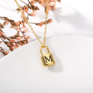 Detail view of a gold stainless steel lock pendant necklace with engraved letter M detail