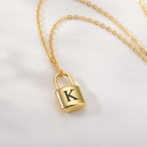 Detail of golden padlock pendant necklace with engraved letter K on a fine chain