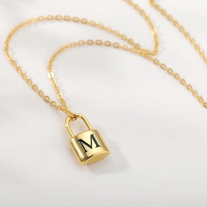 Close-up of golden padlock pendant with engraved letter M and brushed metal finish on chain