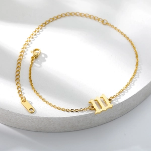 Detail of gold 18K plated stainless steel anklet with gothic letter W pendant on tray
