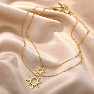 Detail einer goldener Edelstahlschichtkette mit Sonnenanhängern auf Satinhintergrund
