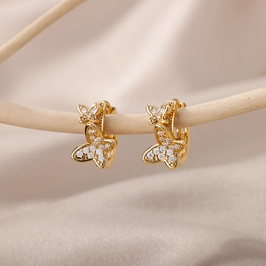 Makroaufnahme goldener Schmetterlingsohrringe mit Zirkon auf hellen Holzzweigen