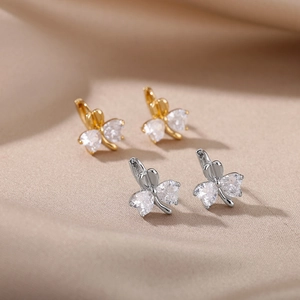 Makroaufnahme goldener und silberner Kleeblatt-Ohrringe mit Herz-Zirkonia auf Satin