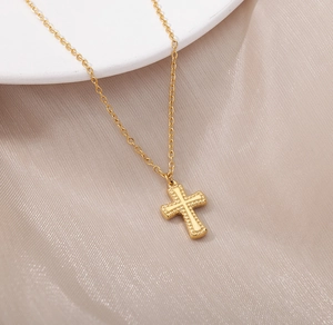 Gros plan d'un pendentif croix en acier doré avec relief sur un tissu de soie champagne