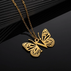Macro shot of gold butterfly necklace with hollow wings and initial V on black mirror