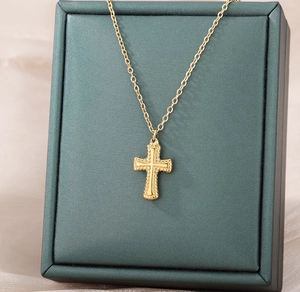 Détail macro du collier croix arbre de vie doré présenté sur un écrin de bijoux vert foncé