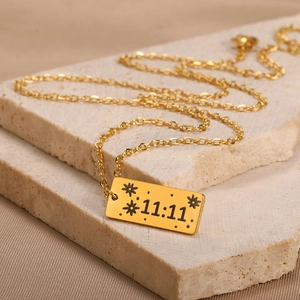 Close-up of 18K gold rectangular pendant with 11:11 engraving on textured stone