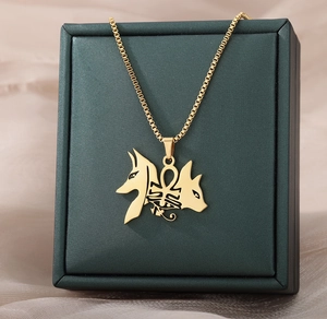 Gros plan d'un collier croix Ankh doré avec têtes d'Anubis sur du satin champagne