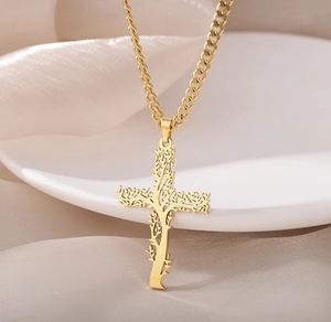 Gros plan sur un pendentif croix arbre de vie doré sur satin blanc et céramique