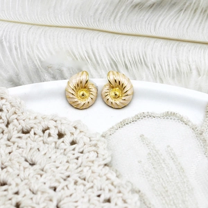 Detail of spiral conch gold stud earrings with cream enamel on white feather background