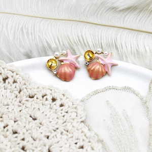 Close-up of pink shell and starfish earrings with pearls on white lace background
