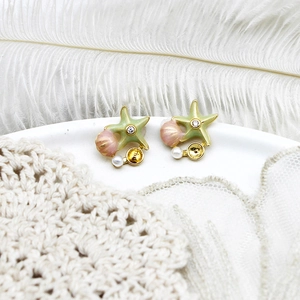 Detailed shot of starfish and seashell earrings with pearls on a decorative white dish