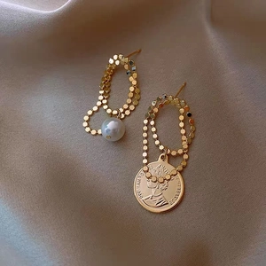 Detail showing asymmetric gold earrings with pearl and queen coin charms on satin
