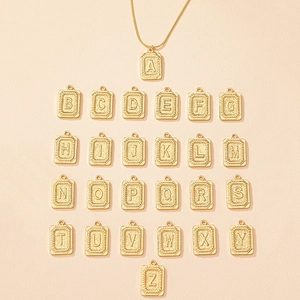 Macro detail of gold initial rectangle pendants with embossed letters on sand background