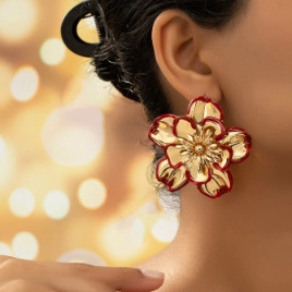 Close-up of oversized gold flower earrings with red enamel edges on female model