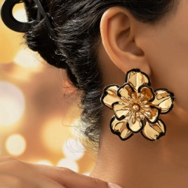 Close-up of golden floral stud earring with black enamel outline on model's ear