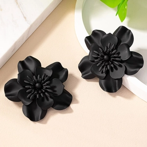 Detailed close-up of matte black floral stud earrings on a minimalist marble background