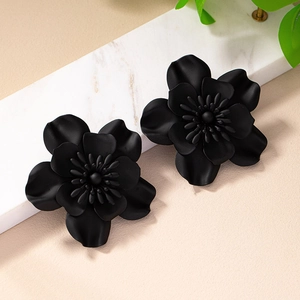 Fashionable matte black flower earrings with layered petals on a marble display