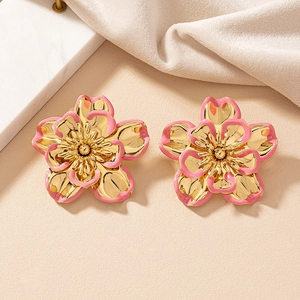 Close-up of elegant gold flower earrings with pink enamel petals on marble background
