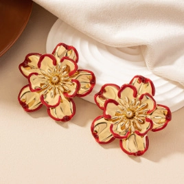 Detail of vintage 3D flower earrings with red enamel edges on a white ceramic plate