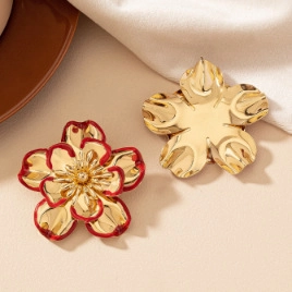 Close-up of elegant gold and red enamel flower earrings on a textured fabric background