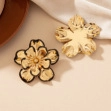 Macro detail of gold-plated flower earrings with black borders and textured petals
