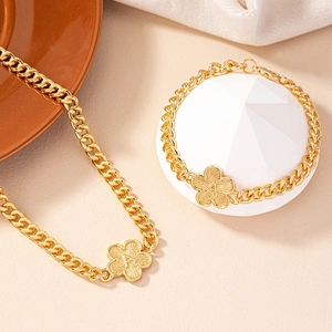 Golden Cuban chain jewelry set with flower alphabet pendants on a warm elegant background