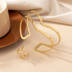 Detailed view of minimalist gold wave bangle and matching ring set on beige background