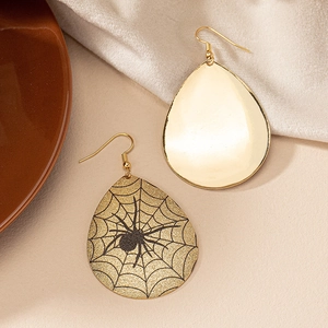 Detailed close-up of gold teardrop earrings featuring a black spider web and spider motif