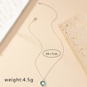 Detailed close-up of a silver heart pendant necklace with green stone on marble