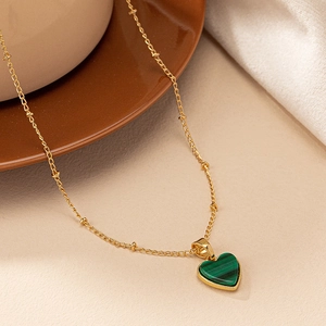 Detail shot of a green malachite heart pendant on a delicate beaded gold chain