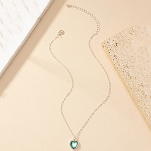 Detail of silver heart necklace with green gemstone pendant and lobster clasp on marble
