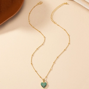 Elegant gold heart necklace with dark green malachite texture pendant on beige background