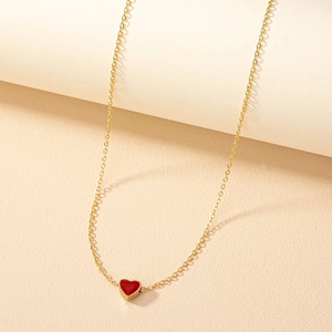 Collier en or minimaliste avec pendentif cœur rouge vif sur un fond esthétique beige neutre