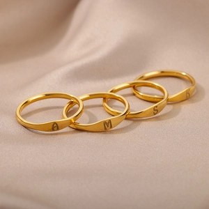 Detailed shot of four gold-plated initial rings A, M, S, K on champagne silk fabric