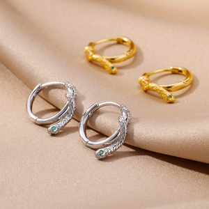 Macro detail of gold and silver snake hoops with green zircon eyes on silk fabric