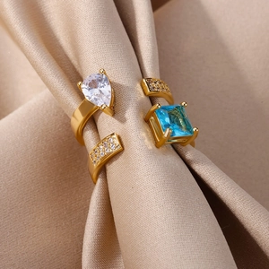 Detail of gold open ring featuring teardrop zircon and blue square stone on satin