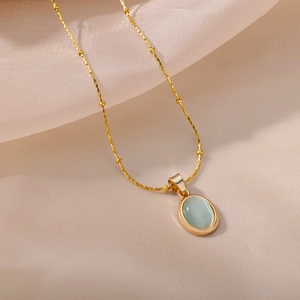 Detail view of gold beaded chain and oval light green cat eye stone pendant on silk fabric