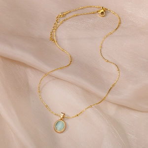 Detail of gold oval pendant with light blue gemstone on champagne satin silk background
