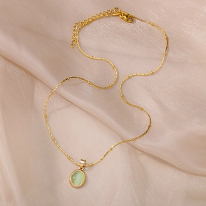 Detailed shot of golden necklace with green cat-eye pendant on beige satin background