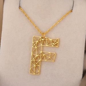 Detailopname van de gouden holle letter F hanger met geometrisch raster en fijne ketting