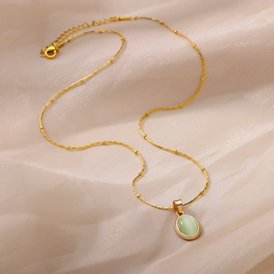 Detail of a gold titanium necklace with oval cat-eye stone pendant on silk fabric