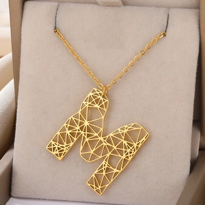 Detailopname van de holle geometrische gouden letter M hanger aan een fijne ketting