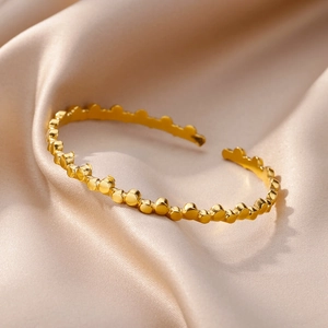 Close-up of golden stainless steel open bracelet with textured bead dot design on silk