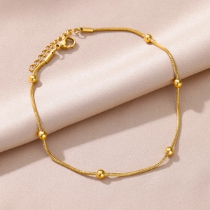 Detailed close-up of a gold-plated snake chain anklet with polished beads on satin