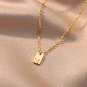 Macro detail of gold square pendant with letter M on soft champagne satin fabric
